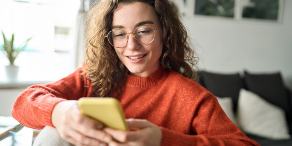 Woman in red jumper researching on her phone about generative engine optimisation - The PHA Group
