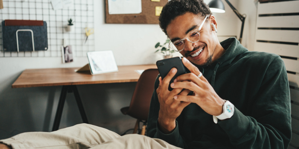 Man sitting on sofa looking at his phone smiling at GEO integrated into his digital strategy - The PHA Group 