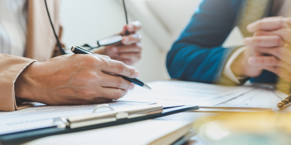 Man writing on paper sitting next to a client in a suit - The PHA Group