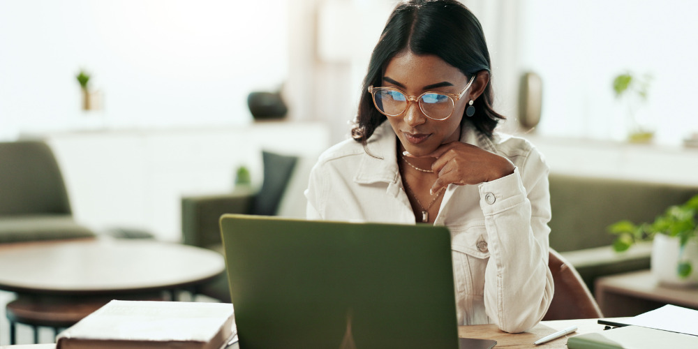 Woman sitting at desk with glasses on looking at a laptop where she has written a press release for IA visibility - The PHA Group
