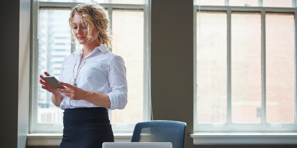 Female lawyer standing behind her desk in an office on her phone - The PHA Group
