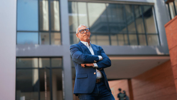 Business man in suit standing outside a building with his arms crossed - The PHA Group