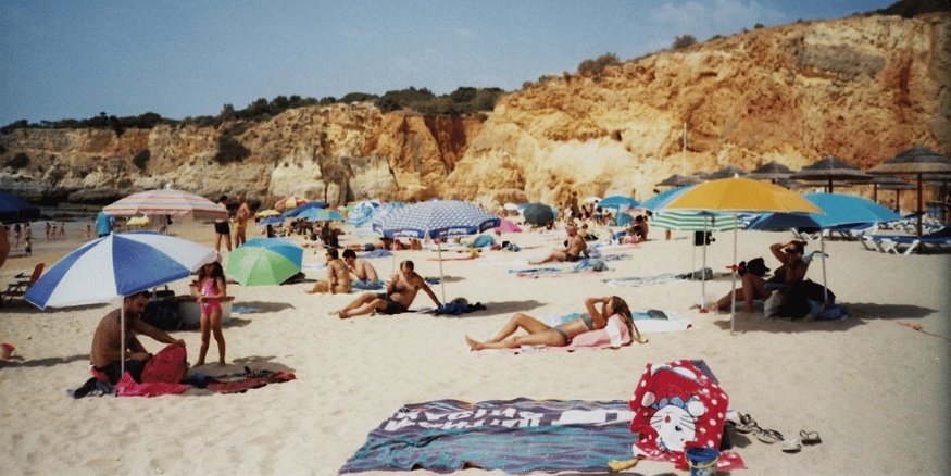 Crowded sandy beach with people laying under umbrellas - The PHA Group