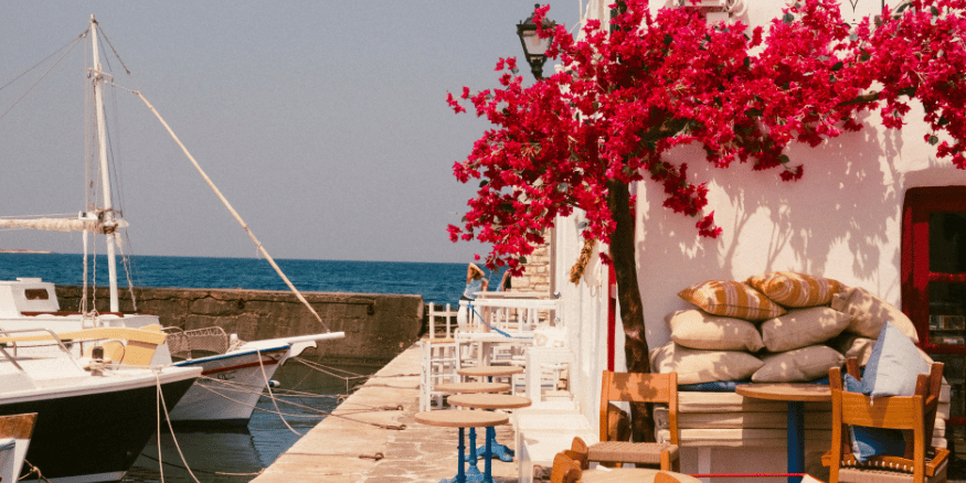 Scenic photo of greek island with white house and pink flowers next to a boat - The PHA Group