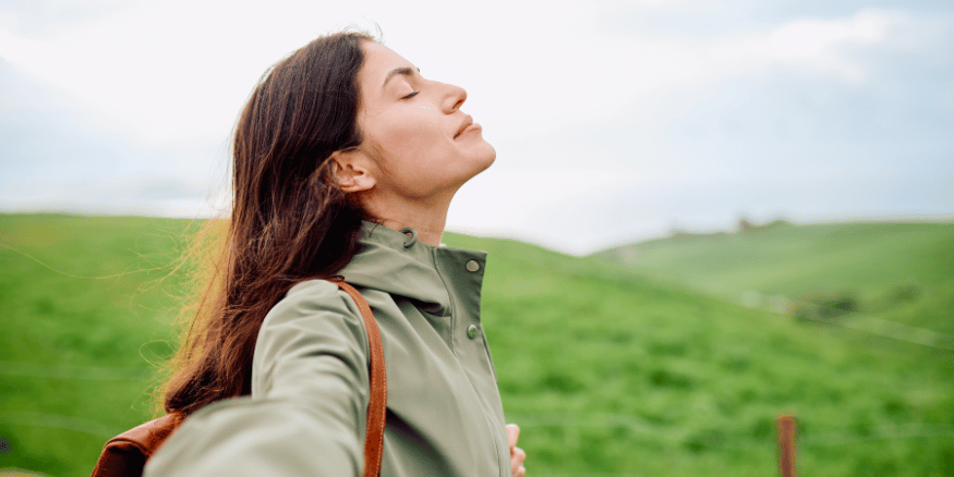 Woman inhaling fresh area in a green field while on a sustainable holiday - The PHA Group