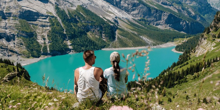 Couple sitting on a cliff edge looking at the mountain view and a lake - The PHA Group