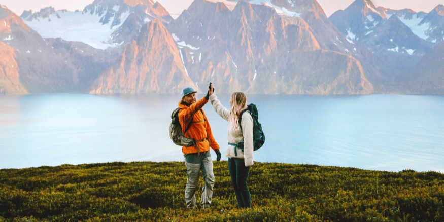 Man and woman high-fiving at the end of their sustainable hiking holiday in the mountains in front of a lake - The PHA Group